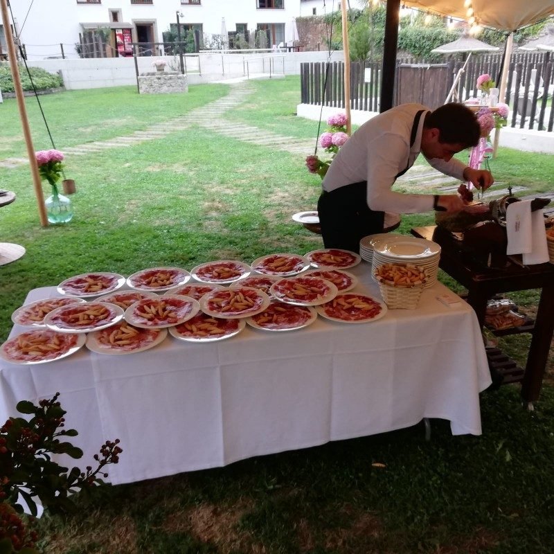 Mesa de buffet con platos de jamón bajo carpa en un jardín